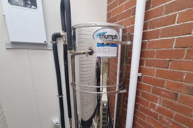 Custom marine-grade stainless steel hot water cylinder installed against a brick wall at a Wellington home