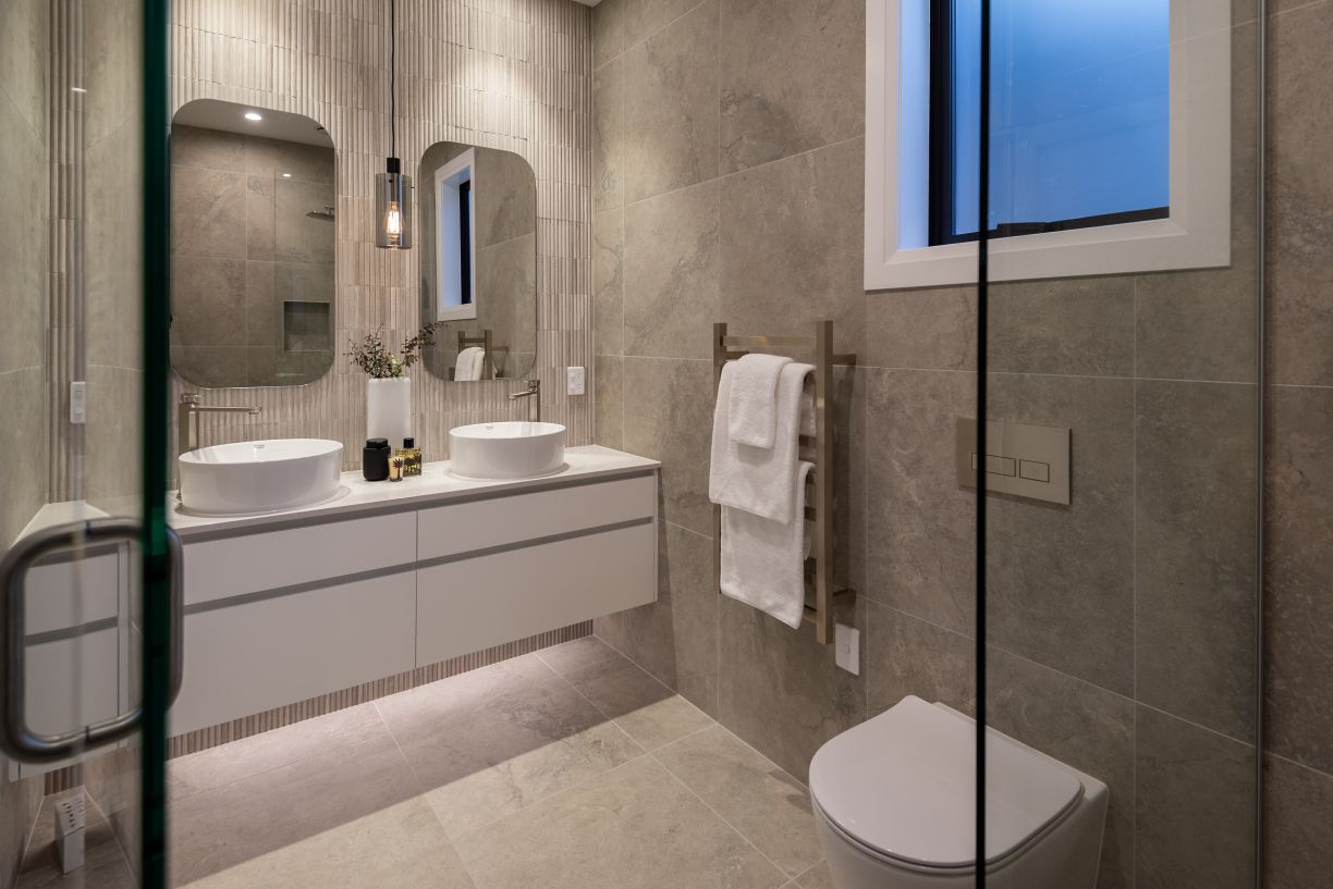 A luxury master bathroom renovation completed by Level Plumbing Howick. The modern space features a floating white double vanity with twin ceramic vessel basins and contemporary chrome taps. The design includes an in-wall concealed toilet cistern with a m
