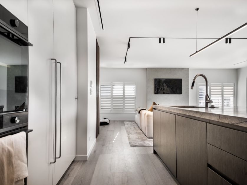 An open-plan kitchen and living space fit-out by Level Plumbing Howick, featuring a premium stainless steel kitchen faucet mounted on a stone island countertop next to white integrated appliances.