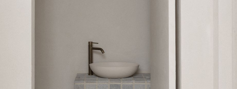 A minimalist modern bathroom renovation in Howick, Auckland, featuring a custom tiled floating vanity counter, light stone vessel sink, and an elegant brass tap against textured plaster walls.