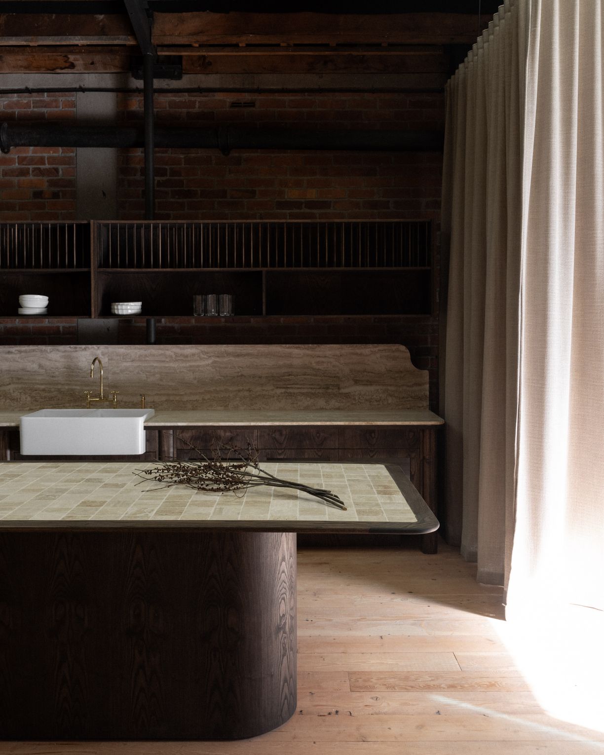 A high-end kitchen fit-out and plumbing installation in East Auckland by Level Plumbing Howick, featuring a classic white farmhouse apron-front sink, travertine countertops, and a custom dark wood island.