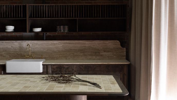 A high-end kitchen fit-out and plumbing installation in East Auckland by Level Plumbing Howick, featuring a classic white farmhouse apron-front sink, travertine countertops, and a custom dark wood island.