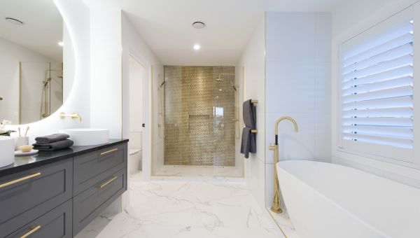 A full view of a luxury bathroom installation completed by Level Plumbing Howick. The space features a white freestanding bath with a floor-mounted brass filler tap, a large dark grey double vanity with dual vessel sinks, and a walk-in shower enclosure hi