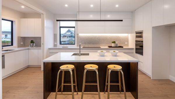 A straight-on view of a luxury kitchen and scullery renovation completed by Level Plumbing Howick. The open-plan layout showcases a dark timber island bench with a white stone countertop, an undermount square stainless steel sink, a modern chrome mixer ta