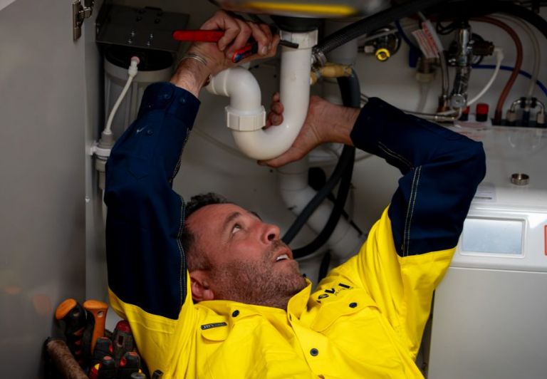 A professional plumber working on residential under-sink PVC drainage pipes and plumbing systems.