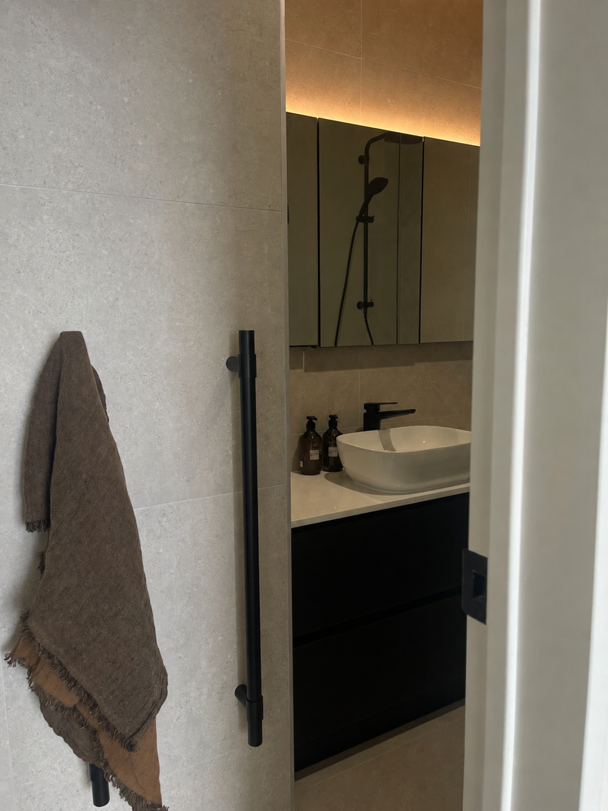 Modern ensuite bathroom renovation in Howick featuring a vertical black heated towel rail, floating vanity with white vessel basin, black mixer tap, and illuminated mirror cabinet installed by Level Plumbing Howick.